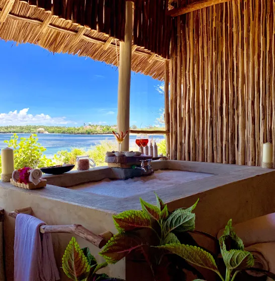 A private soaking tub under a makuti roof, set with candles and a glass of wine, looking out over Mida Creek