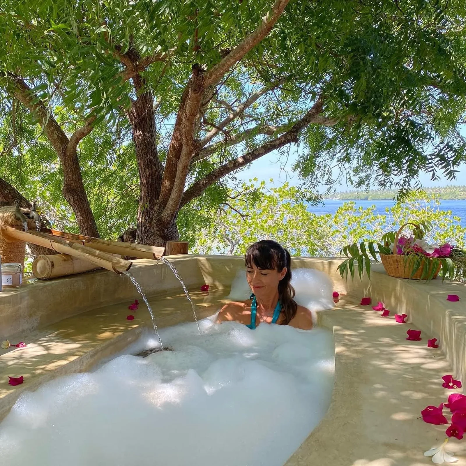 A bath scattered with bougainvillea petals in the shade of a tree, the creek just beyond