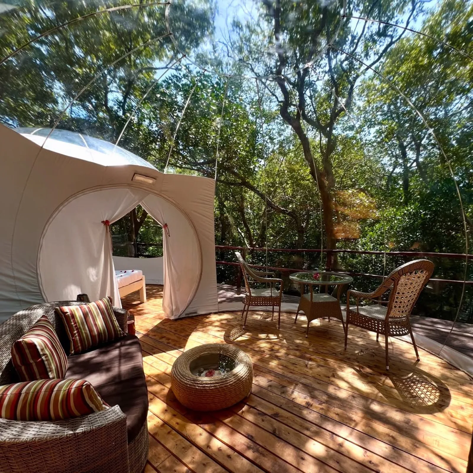 A private deck inside a bubble lodge among the trees, with two chairs set for a quiet afternoon